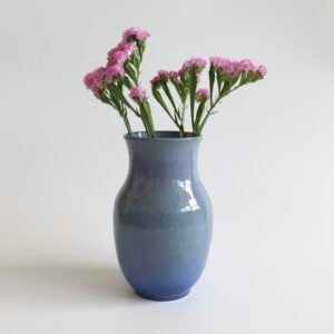 Hangedraaide keramieke vaas in grijs-blauw met glanzend glazuur, gevuld met roze anjers.