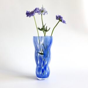 Vintage glazen vaas met golvende vorm en blauwe vlekkenpatroon, gevuld met paarse bloemen.