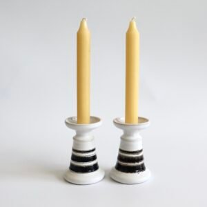 Set van twee vintage Strehla keramische kandelaars in wit met zwarte strepen, elk met een gele kaars.