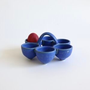 Vintage Deense eierhouder van blauw aardewerk met vijf komvormige vakken en centrale handgreep, met rood ei.