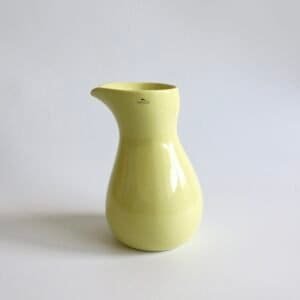 Gele Kähler Mano pitcher met glanzend geglazuurd oppervlak, klassieke vorm met uitsnede aan de rand en gebogen hengel.