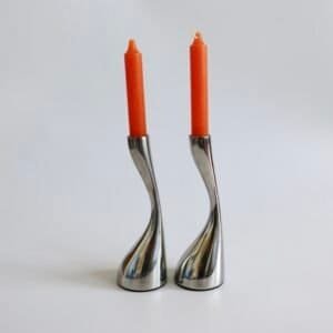 Twee roestvrijstalen kandelaars met golvende vorm en rode kaarsen, vintage design.