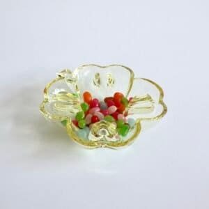 Vintage geel glazen catch-all schaaltje in bloemvorm, gevuld met gekleurde glaskralen in rood, groen en roze tinten.