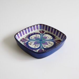 Royal Copenhagen vintage fajance schaal met vierkante vorm, blauwe rand en decoratief patroon met paarse bloemmotief in het centrum.