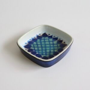 Vintage Royal Copenhagen fajance schaal met blauw geometrisch patroon en bladmotief aan de rand, midcentury design.