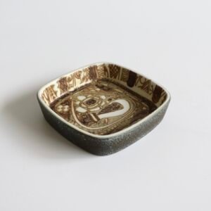 Royal Copenhagen fajance schaal met abstract gezicht en decoratief patroon in bruin op wit, vierkante vorm met geruwde buitenkant.