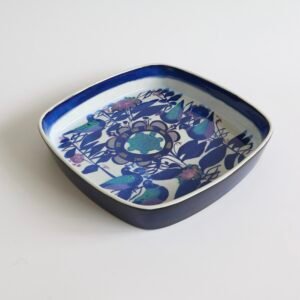 Vintage Royal Copenhagen fajance schaal met afgeronde vierkante vorm, blauw-witte glazuur en botanisch decor in donkerblauw met gekleurde accenten.