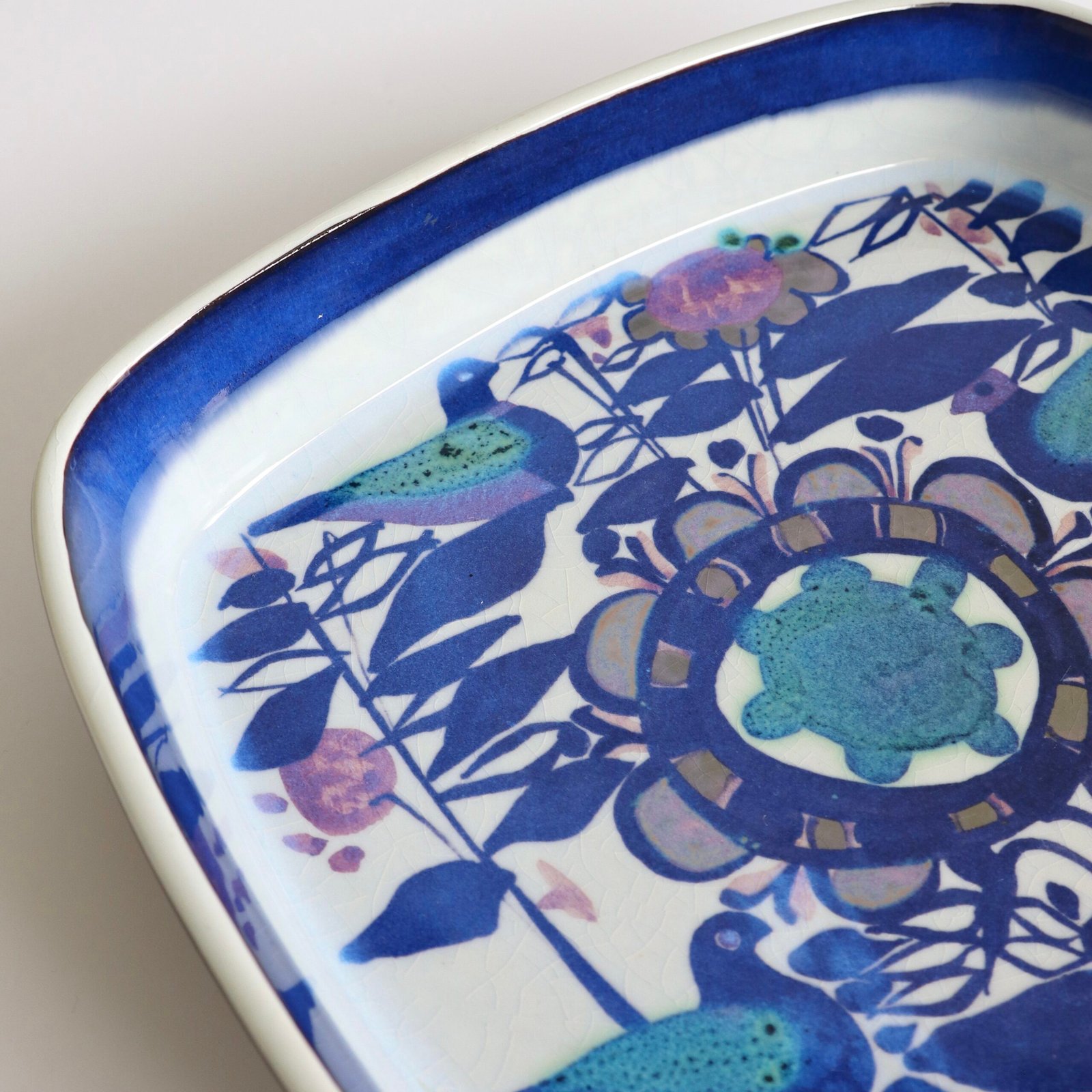 Bovenaanzicht Royal Copenhagen Fajance schaal met vogels, bladeren en ornamentale motieven in blauw en paars.
