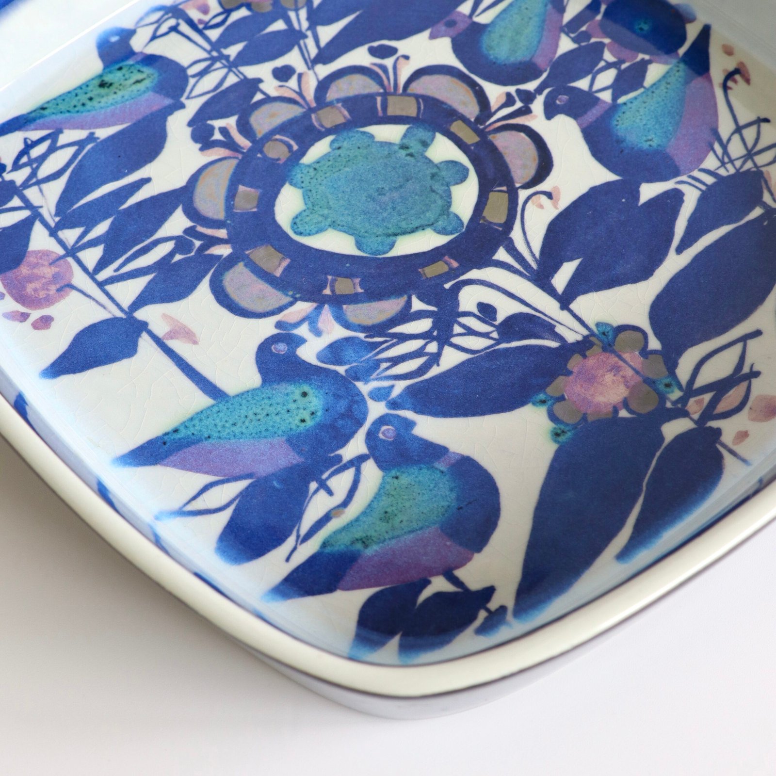 Close-up van Royal Copenhagen schaal met gestileerde vogels en decoratieve bloemen in tinten blauw en paars.