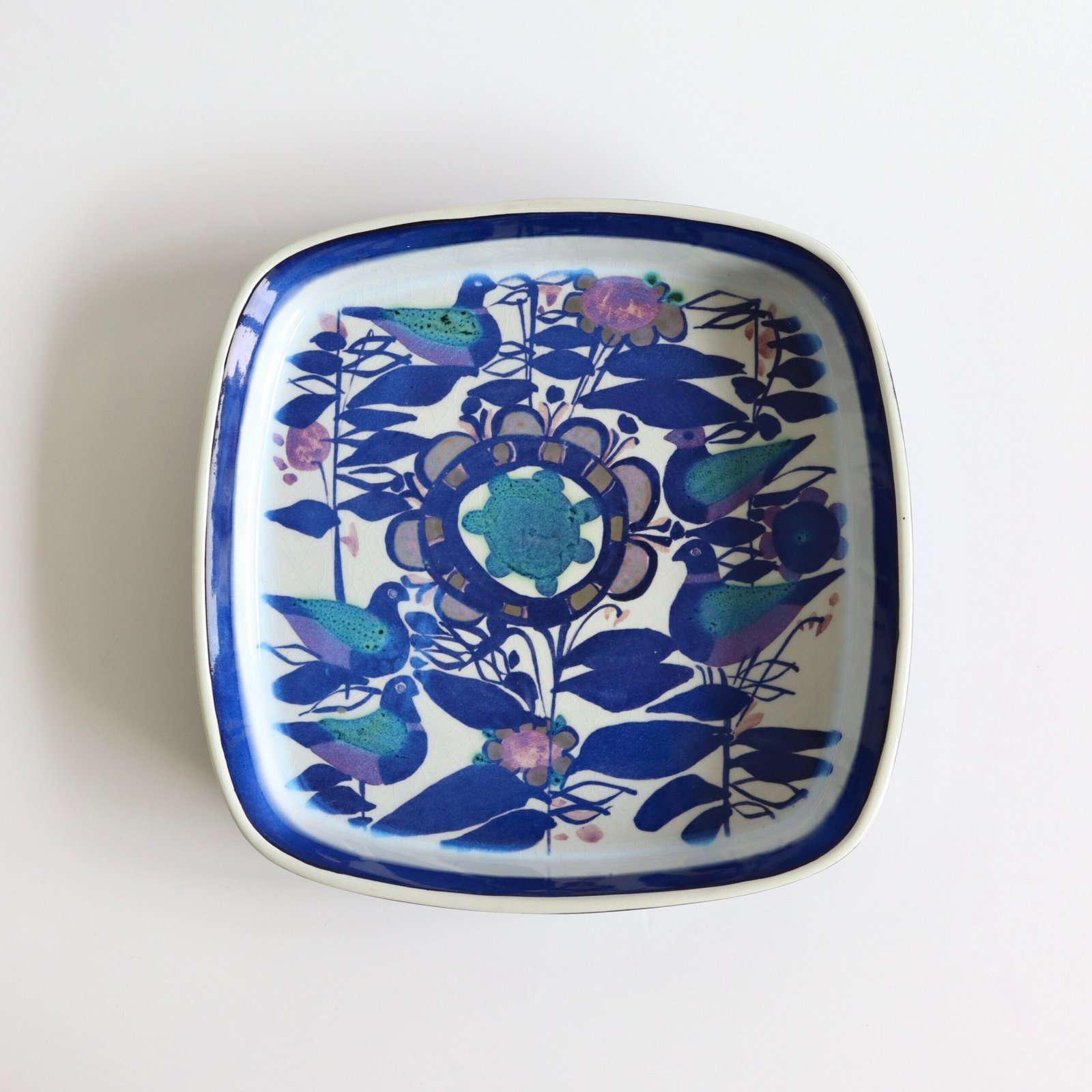 Royal Copenhagen keramische schaal met Kari Christensen vogelmotief in blauw, groen en paars op crème fond.