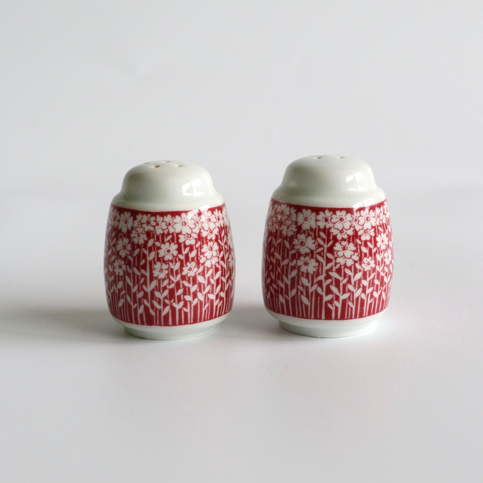 Vintage peper- en zoutstel in rood-wit porselein met bloemetjes- en takjespatroon, twee identieke potjes met witte deksels.
