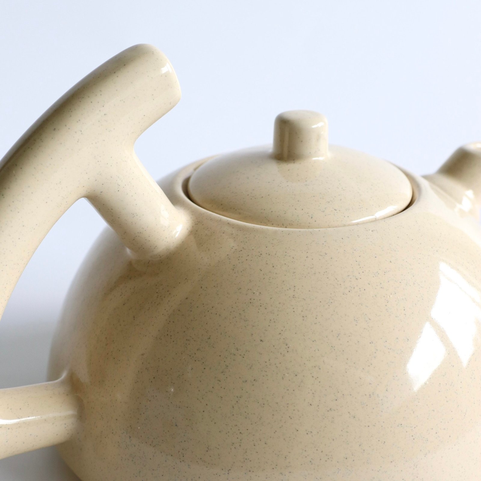 Detailweergave van het beige aardewerk met zichtbare spikkeltjes en handvat van de theepot.