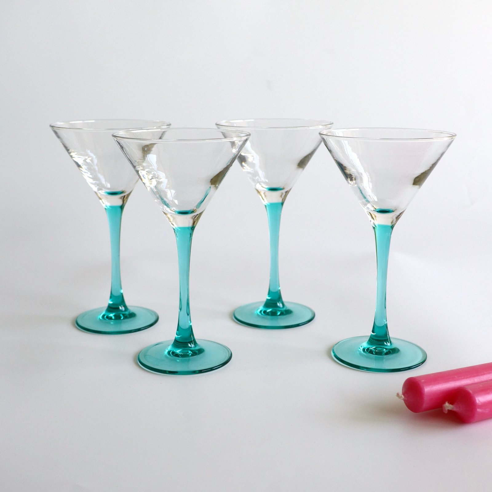Set van vier Luminarc cocktailglazen met turquoise glazen voet en transparante kom, voorzien van decoratieve witte streeppatronen.
