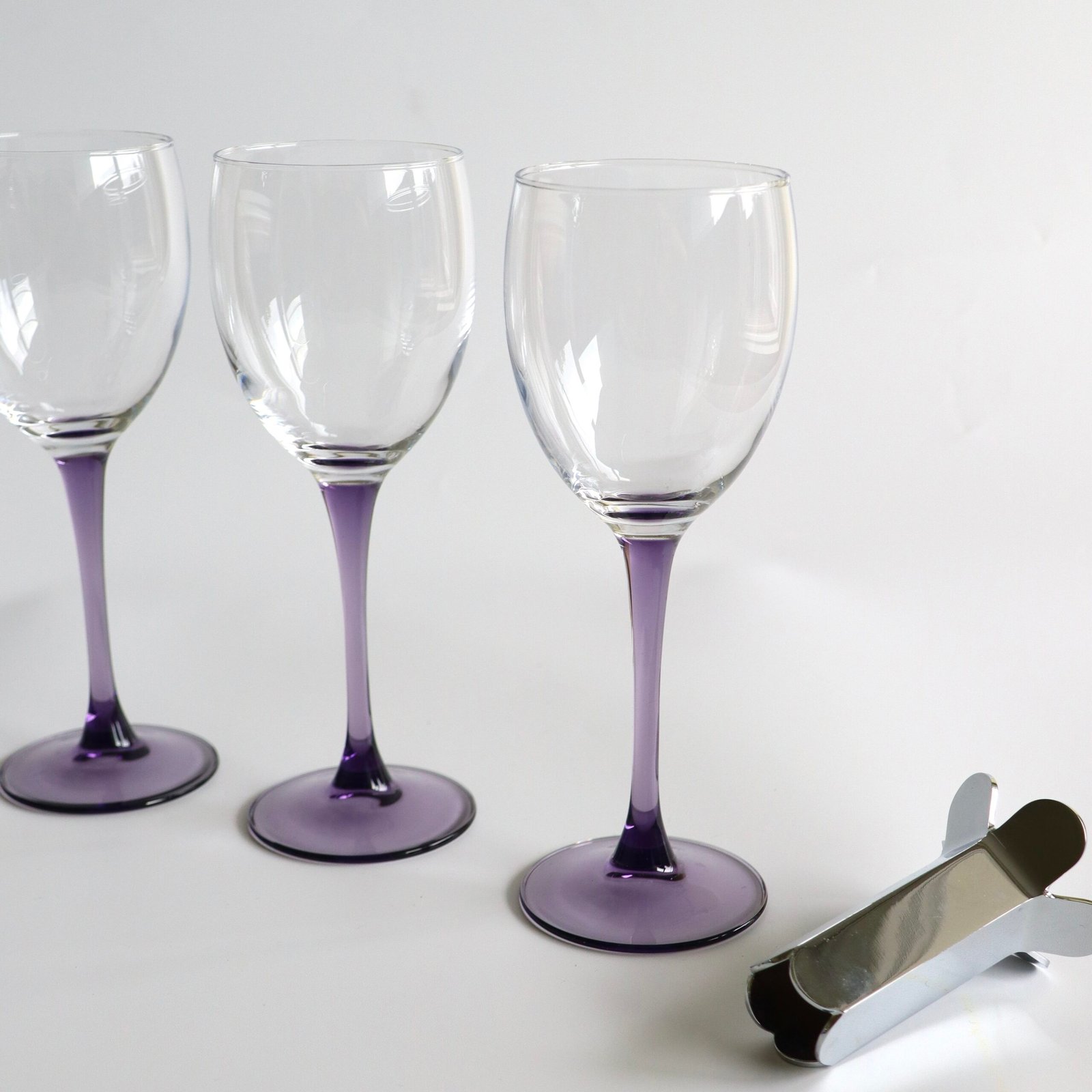 Drie Luminarc France wijnglazen met helder glas en paars gekleurde voet en steel.